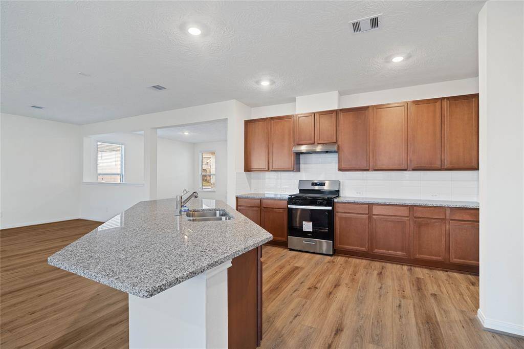 This spacious kitchen features high ceilings, stained wood cabinets, granite countertops, SS appliances, modern tile backsplash, recessed lighting, large kitchen island with space for a breakfast bar, large windows with privacy blinds, and a pantry all overlooking your huge family room.