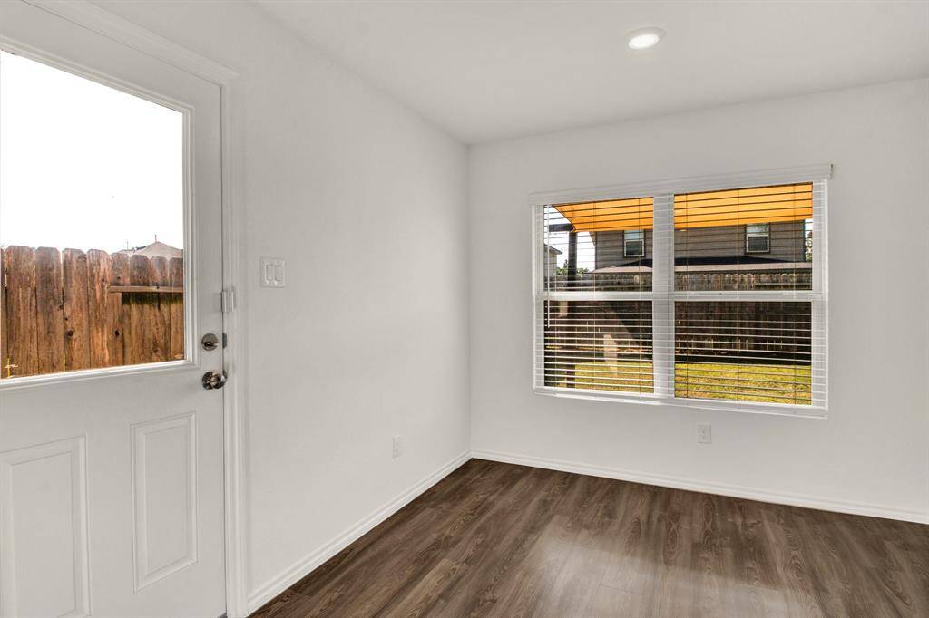 Bright room with hardwood-style vinyl flooring, a large window with blinds, and a door leading to a fenced backyard.