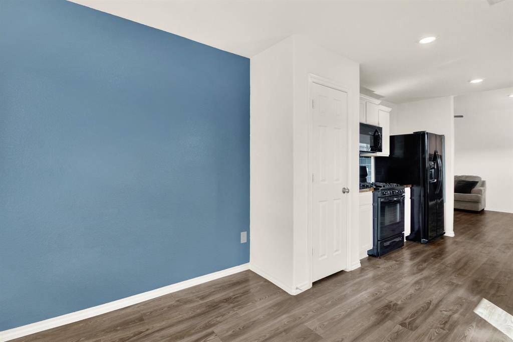 Modern kitchen with sleek black appliances, white cabinetry, and a contrasting blue accent wall. The space has wood flooring and recessed lighting, creating a cozy and contemporary atmosphere.