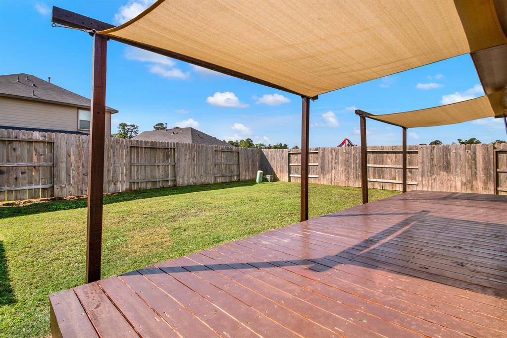 Spacious backyard with a wooden deck and shade sails, enclosed by a wooden fence. Perfect for outdoor relaxation and entertaining.