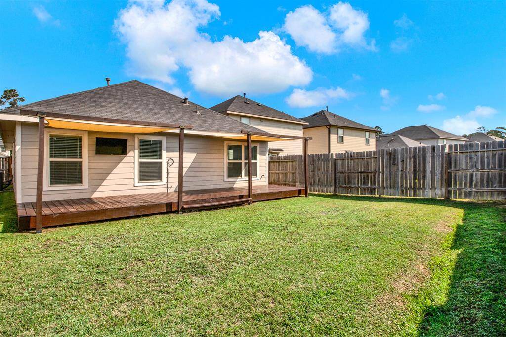 Spacious backyard with a well-maintained lawn and a wooden deck attached to the house. The area is enclosed by a wooden fence, providing privacy and a great space for outdoor activities.
