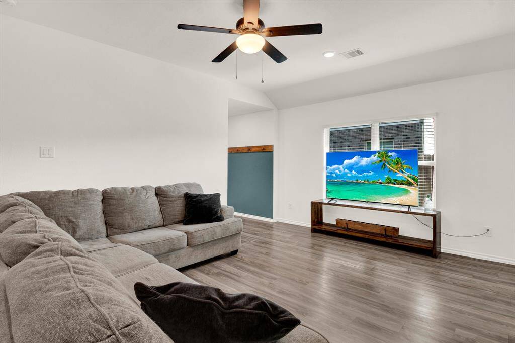 This living room features a cozy gray sectional sofa, hardwood-style vinyl flooring, and a ceiling fan. A large window lets in natural light - perfect for relaxation