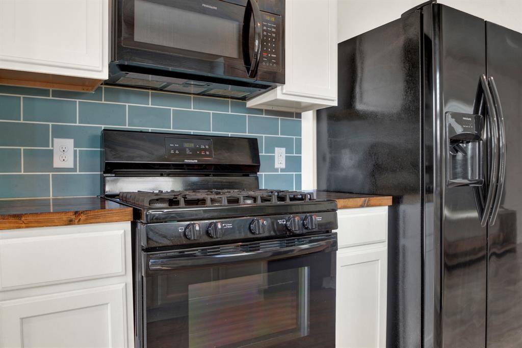 Modern kitchen with sleek black appliances, including a stove and refrigerator. Features a stylish blue subway tile backsplash and white cabinetry, creating a clean and contemporary look.