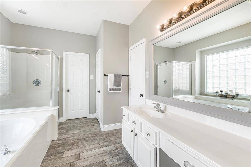 This luxurious ensuite offers wood-look tile flooring, a relaxing jetted tub, a walk-in shower, dual vanities, and a private water closet.