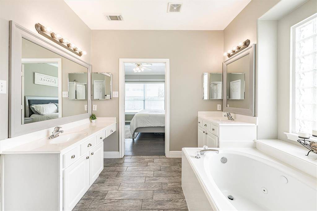 The owner's ensuite bathroom is easy to share with two separate vanities. Each has a custom framed mirror with vanity lights above and one vanity offers knee space to sit while you primp.