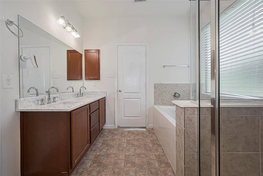 This bathroom features a double vanity with marble countertops, ample cabinetry, a large mirror, and bright lighting. It includes a separate shower, a spacious bathtub, and a window for natural light. The neutral tiles and flooring create a clean, modern look.