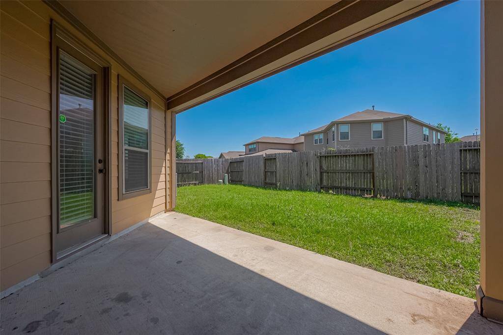 A covered patio leading to a fenced backyard with green grass, perfect for outdoor relaxation and privacy.