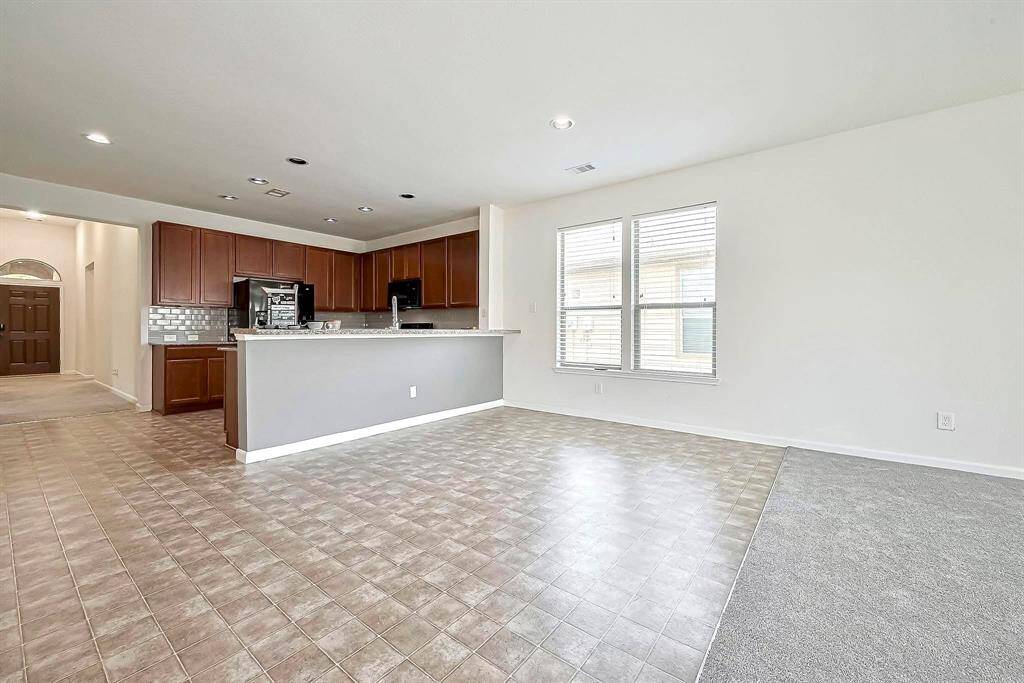 This open-concept living space features a modern kitchen with dark wood cabinets, a sleek backsplash, and a peninsula counter. The area is well-lit with natural light from large windows, providing a cozy yet functional layout.
