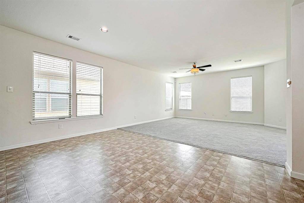 This spacious, open-concept room features large windows for natural light, and a ceiling fan, creating a bright and versatile living area.