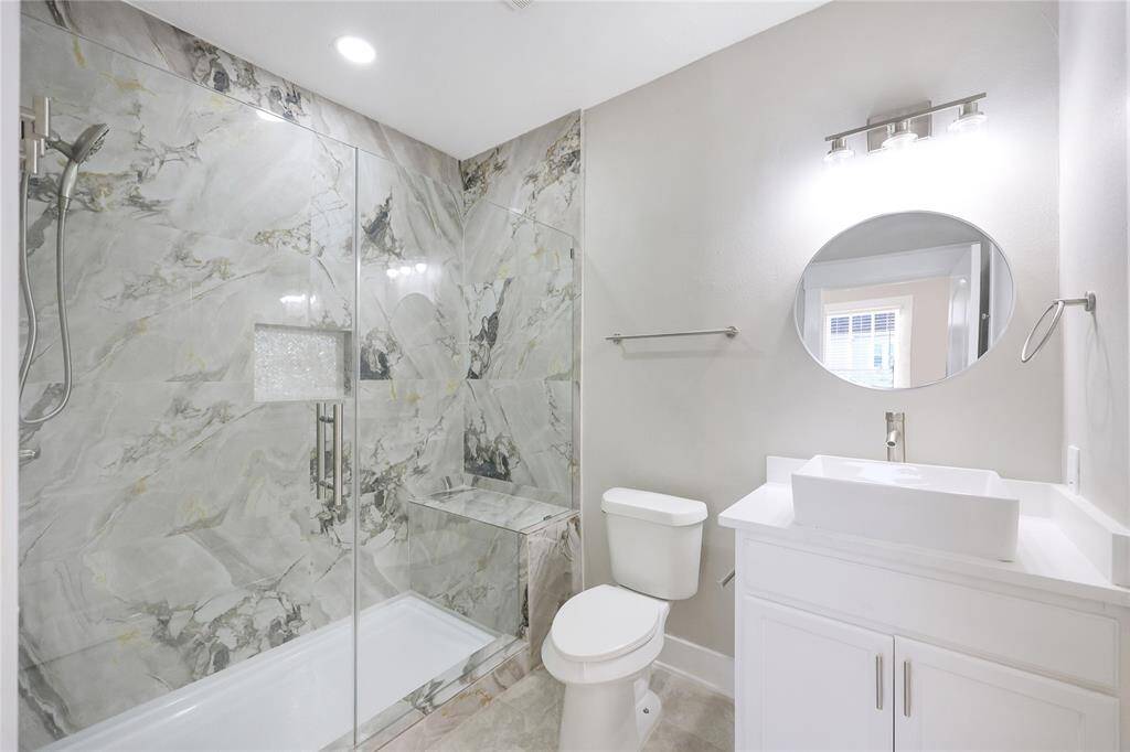 Newly updated primary bathroom features a modern design, featuring a glass-enclosed shower with marble-patterned walls.