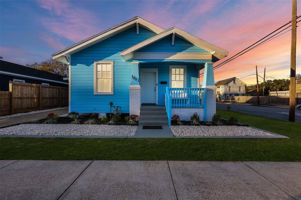 Charming light blue exterior featuring a neatly maintained front yard with a gravel border, a paved walkway, and a small front porch.