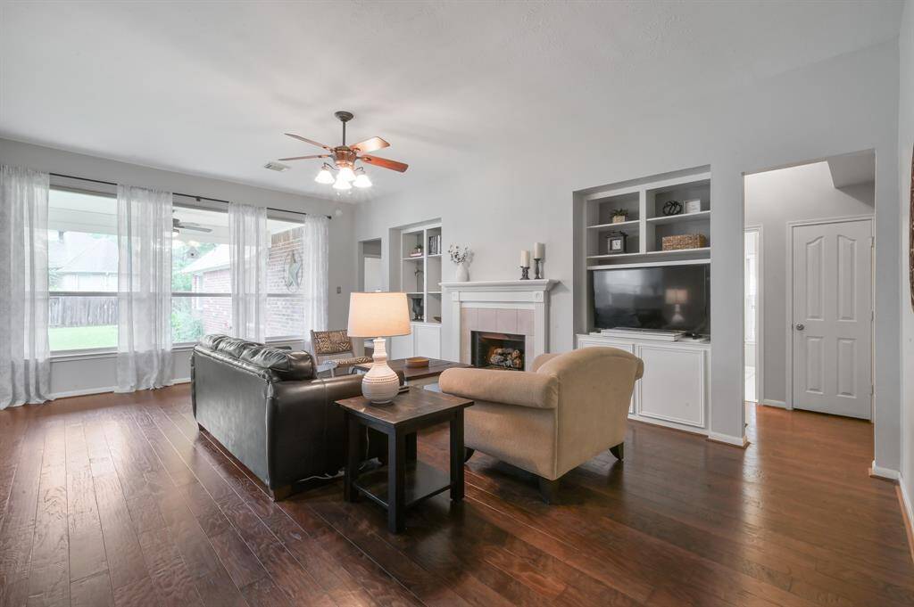 Spacious living room features hardwood floors, a gas fireplace with ceramic logs, and built-in shelving and storage. Large windows with sheer curtains provide ample natural light and there’s plenty of room for additional furniture and configurations to suit your needs.