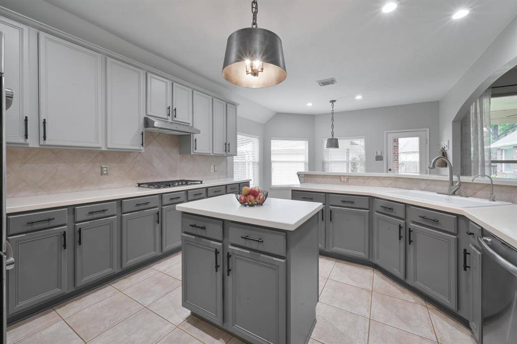Kitchen features modern gray cabinetry, a central island and GE Profile stainless steel appliances. Tile flooring and natural light from breakfast area enhance the open space.