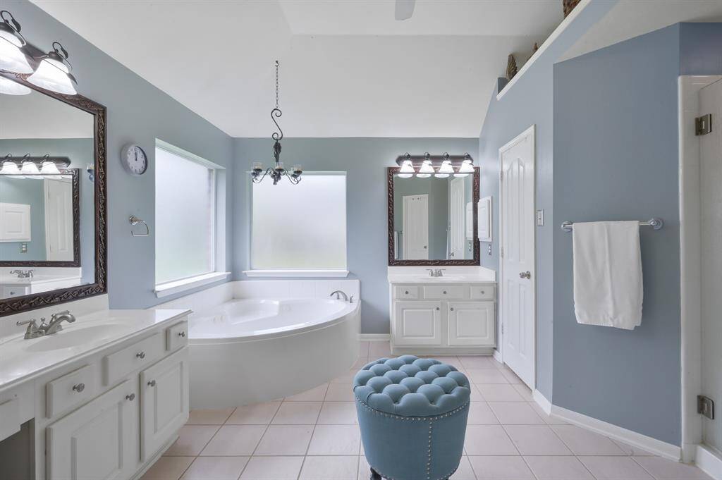 The primary bathroom features a soothing blue color scheme with a large soaking tub, a separate frameless glass enclosed shower and white vanities with framed mirrors. Dual primary closets with Elfa custom shelving systems.