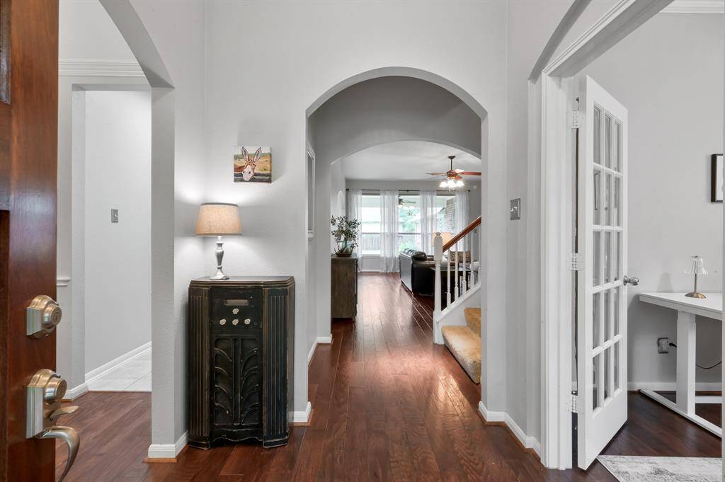Entryway reveals the interior with hardwood floors and Sherwin Williams Agreeable Gray paint throughout the home. A large archway leads to the living area with large windows, a visible staircase with carpeted steps and an office/flex room with French doors on the right.