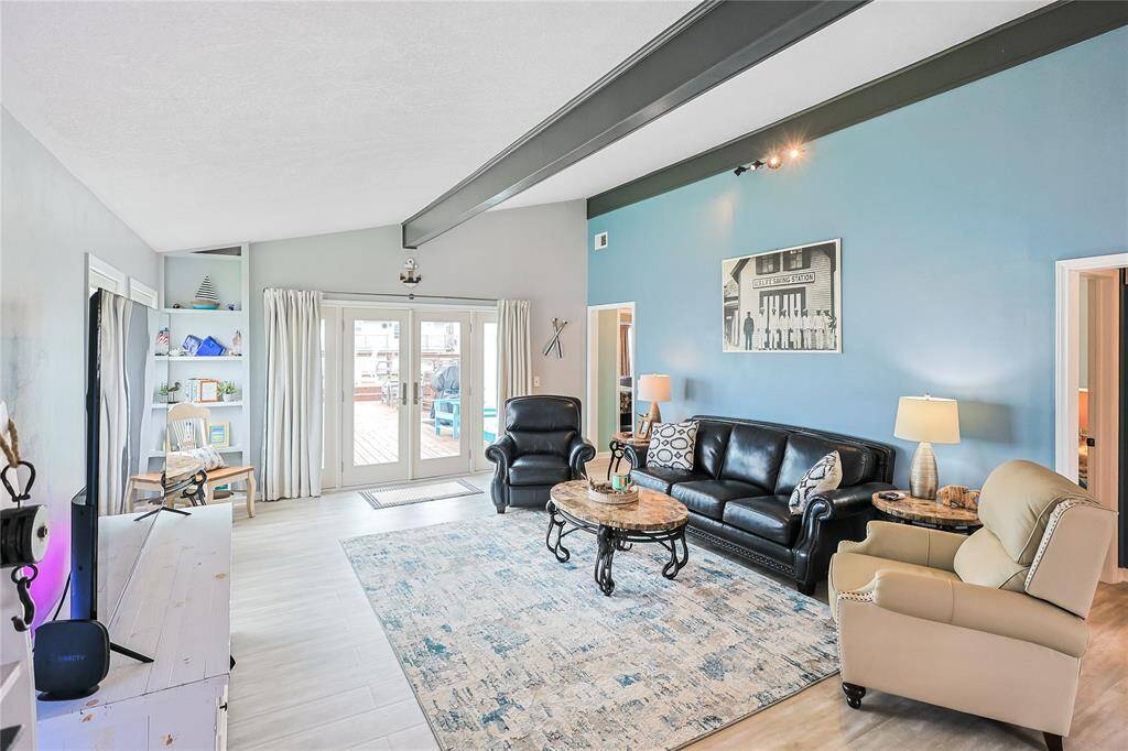 The spacious living room offers vaulted beam ceilings and an abundance of natural light pouring in through the sliding glass door that leads to your private deck overlooking the water.