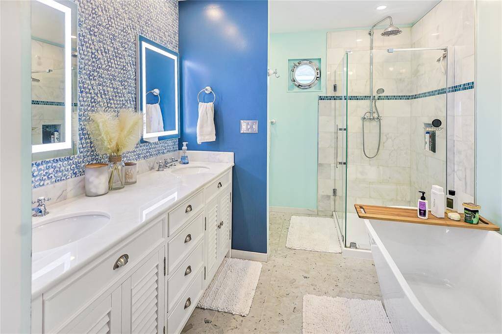 This beautifully updated bathroom includes a spa-like soaking tub, tiled standing shower, his-and-her sinks and a unique porthole window to add to the charm of this waterfront gem!