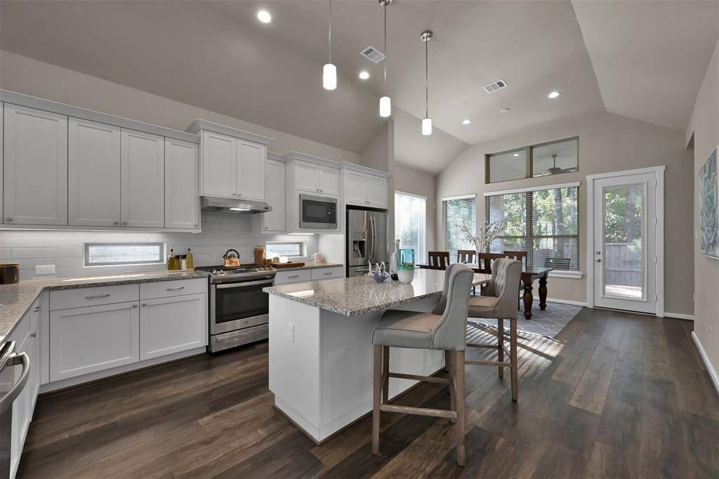 This spacious kitchen features modern white cabinetry, stainless steel appliances, and a large central island with seating. The open layout flows into a bright dining area with large windows and access to a patio, creating an inviting space for entertaining.