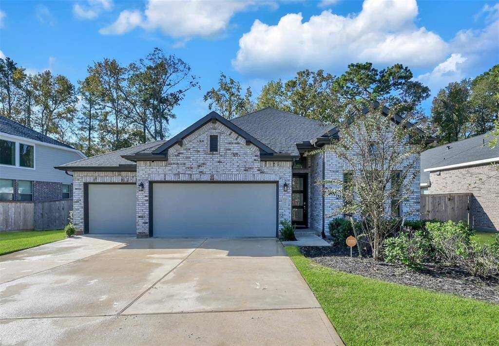 This photo showcases a modern single-story, brick home with a three-car garage. Very few one story with 3 car garages in the community. The house is set against a backdrop of trees, featuring a well-maintained lawn and tidy landscaping. A wide driveway leads up to the garage, providing ample parking space.