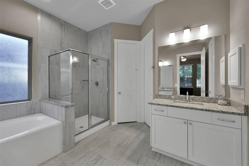 This bathroom features a modern design with a spacious glass-enclosed shower, a large soaking tub, dual sinks with granite countertops, and neutral tile flooring. The space is well-lit with a frosted window for privacy.
