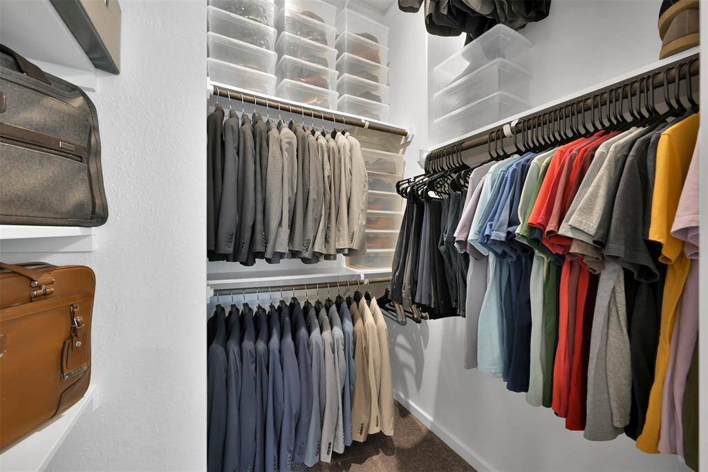 This photo shows a well-organized walk-in closet with ample hanging space for clothes, neatly arranged shirts and jackets, and multiple shelves with storage bins, ideal for keeping your wardrobe tidy.