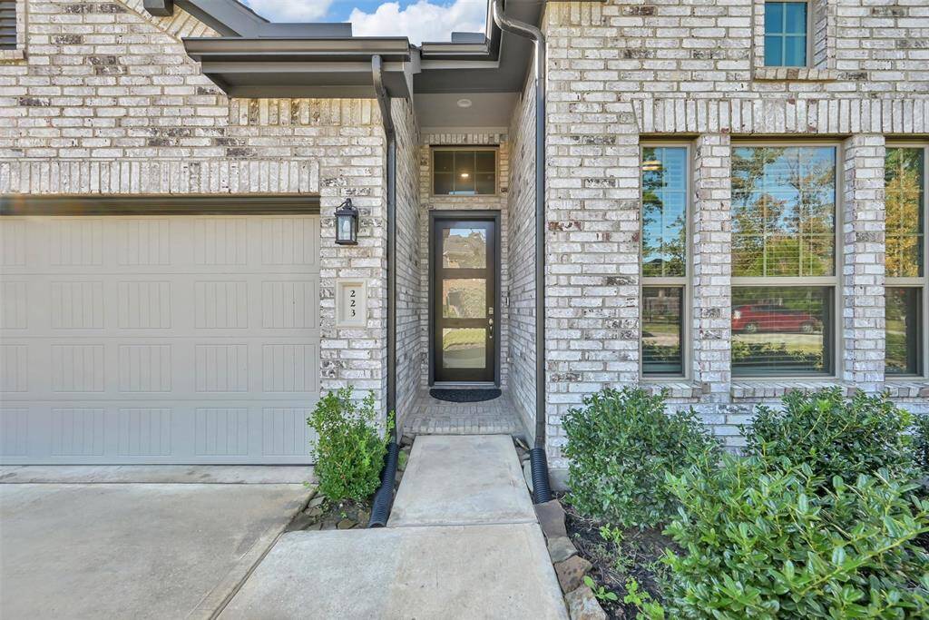 This home features a welcoming entrance with a modern glass door, set between a brick exterior and a tidy front garden. A spacious garage with a stylish door completes the inviting curb appeal.