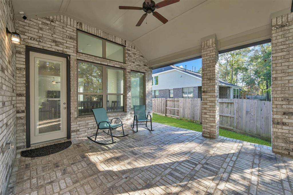 This inviting covered patio features a brick design, ceiling fan, and cozy seating area, offering a perfect outdoor space for relaxation and entertainment.