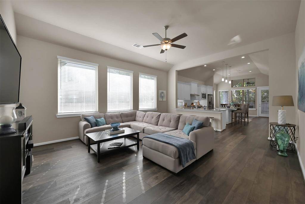 This spacious living area features an open floor plan with large windows for natural light, and a ceiling fan. The adjacent modern kitchen has a large island, white cabinetry, and a dining area, creating a perfect space for entertaining.