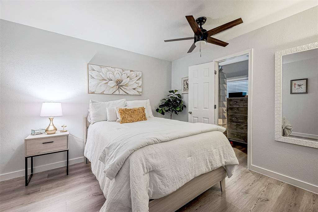 This bedroom offers a cozy and modern feel with neutral tones, a ceiling fan, and ample natural light. It features a comfortable bed, stylish decor, and a large mirror, creating an inviting space.