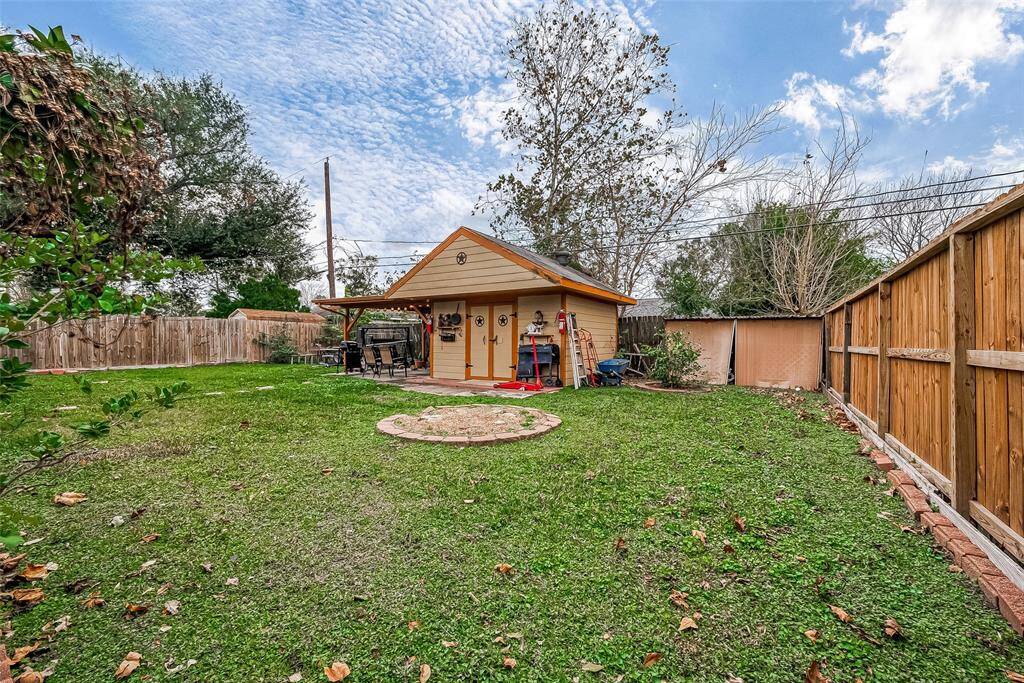 This photo showcases a spacious backyard featuring a well-maintained lawn and a charming wooden shed. The area is enclosed by a wooden fence, providing privacy, and includes a small patio space perfect for outdoor gatherings.