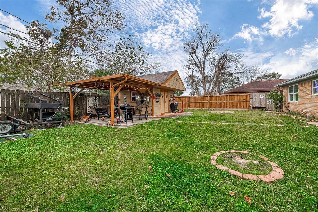 Spacious backyard featuring a charming wooden pergola with seating, perfect for outdoor gatherings. The area is fenced for privacy and includes a well-maintained lawn with stepping stones leading to the pergola. Ideal for relaxation and entertainment.