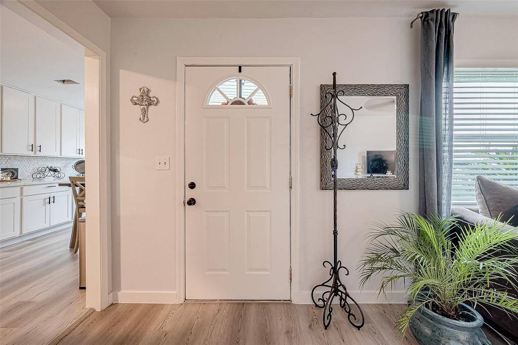 This welcoming entryway features a white door with a decorative arch window, light wood flooring, and neutral walls.
