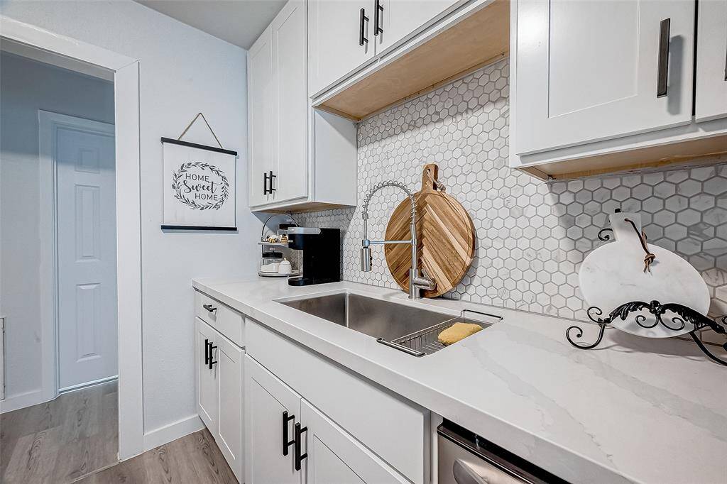 This kitchen features modern white cabinetry with sleek black handles, a stylish hexagonal white tile backsplash, and a quartz countertops. It includes a stainless steel sink with an elegant faucet The space is bright and welcoming, perfect for a contemporary home.