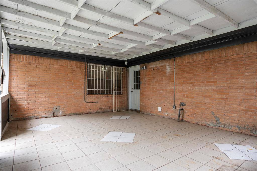 This photo shows a spacious enclosed patio area with tiled flooring and brick walls. The ceiling features exposed beams. Ideal for a versatile indoor-outdoor living space.