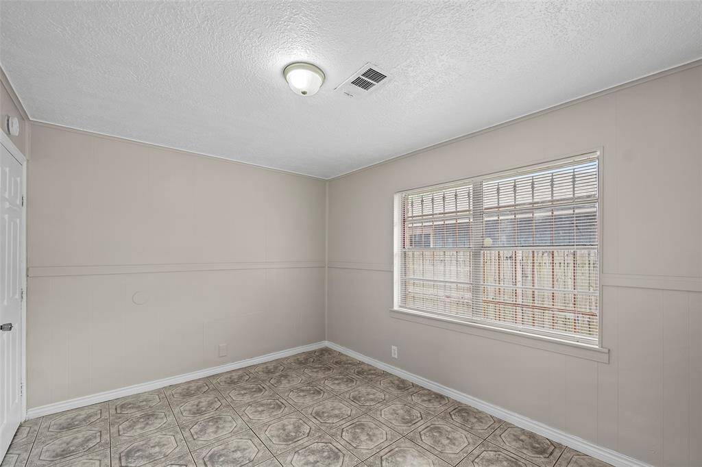 A bright, neutral-toned second bedroom with tiled flooring and a large window that lets in natural light. Perfect for an office or small bedroom.