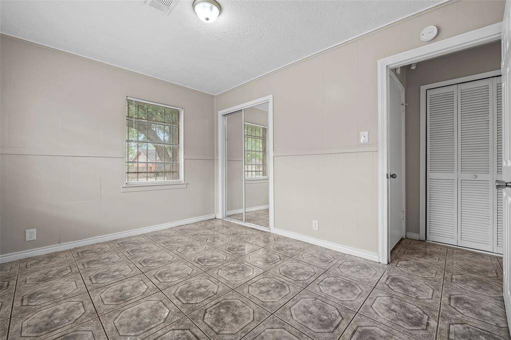 Second room features neutral walls, a patterned tile floor, and ample natural light from the window. It includes a mirrored closet, adding a sense of space.