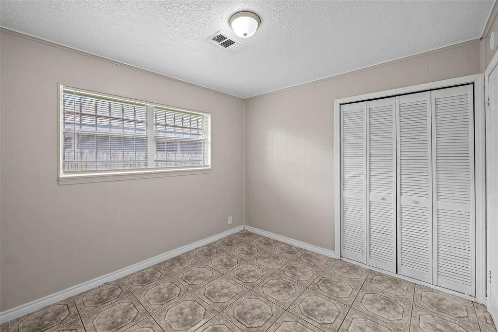 Third bedroom features a neutral color scheme with tiled flooring and a large window that allows natural light. It includes a closet with louvered doors, making it ideal for a bedroom or office space.