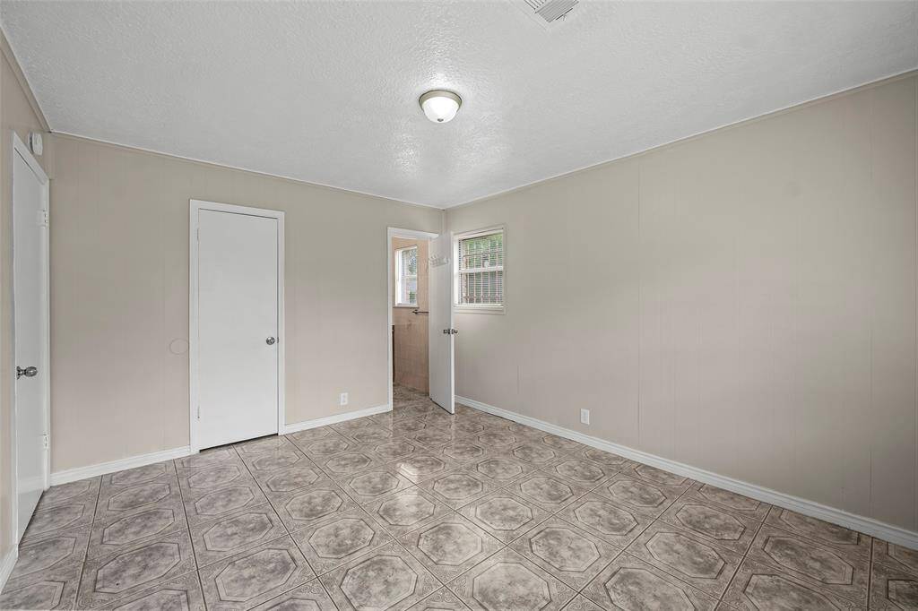 Primary bedroom features neutral-painted walls, a small window for natural light, and patterned tile flooring. It has a ceiling light fixture, walk in closet, and primary bathroom