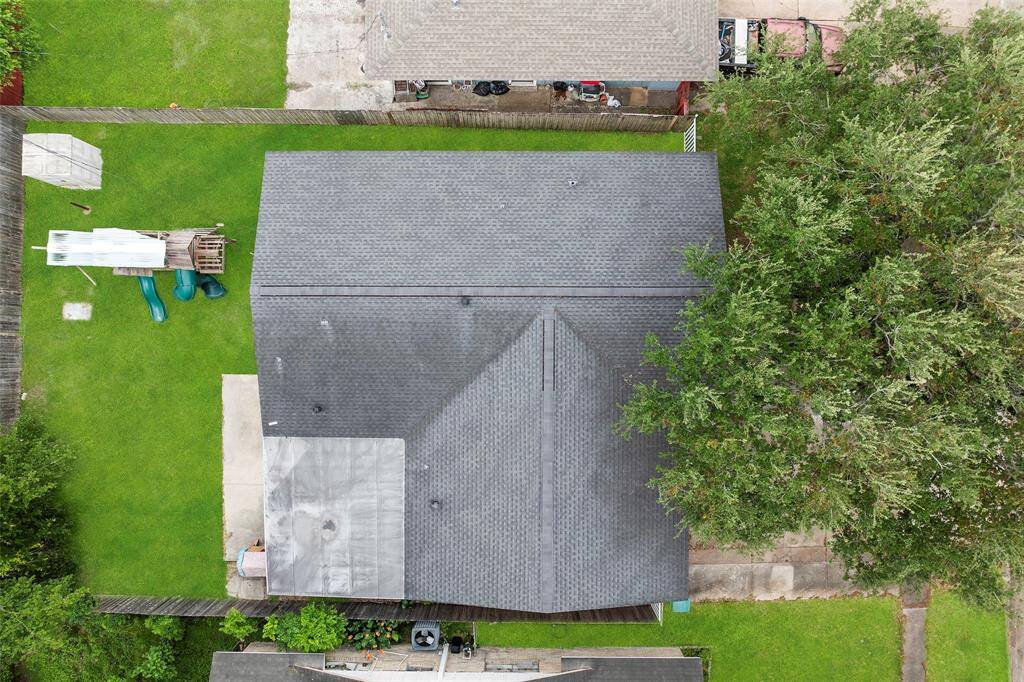 This aerial photo shows a well-maintained house with a dark roof, situated on a green lawn. The backyard features a playset and is bordered by wooden fencing, providing privacy. Large trees add shade and charm to the property.