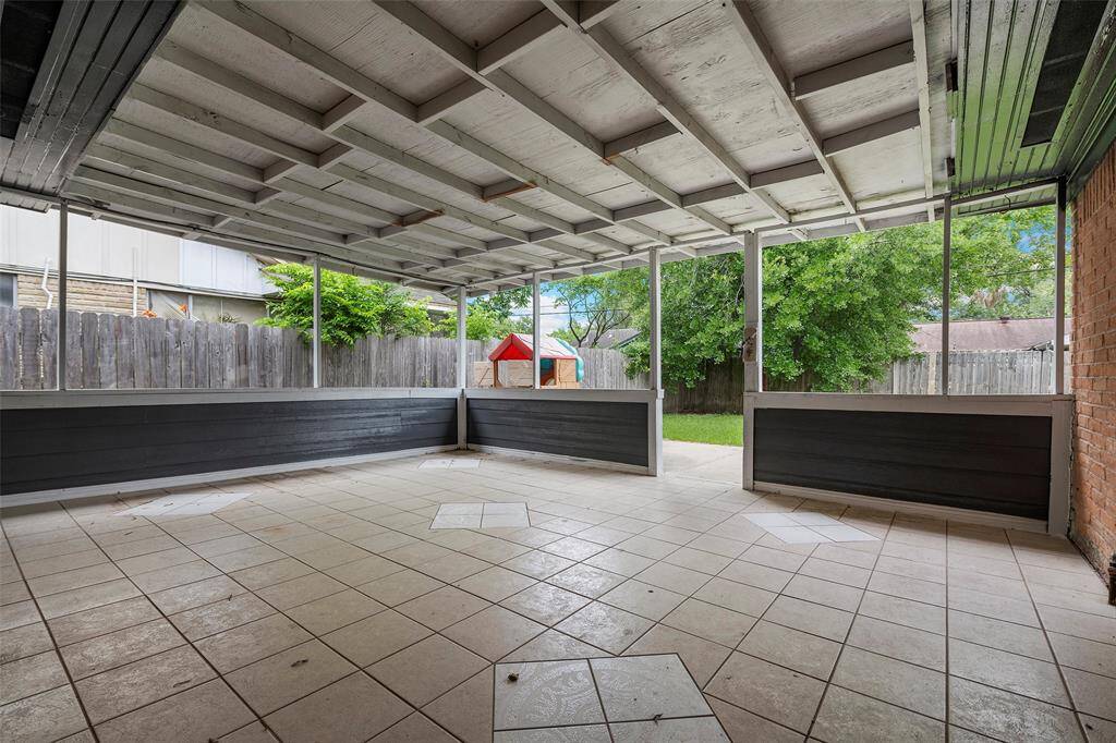This photo shows a spacious, covered patio with tiled flooring, ideal for outdoor relaxation or entertaining. The area opens to a fenced backyard with greenery, providing privacy and a cozy atmosphere.