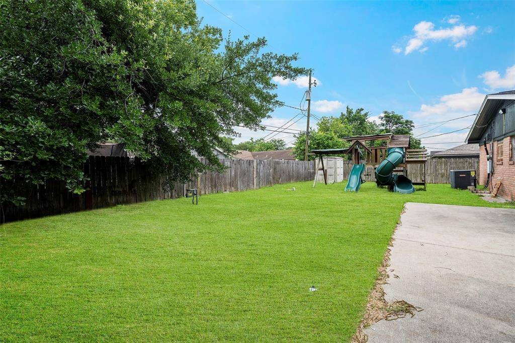 Spacious backyard with well-maintained lawn, a play structure with slides, and a concrete area adjacent to the house. Perfect for families and outdoor activities.