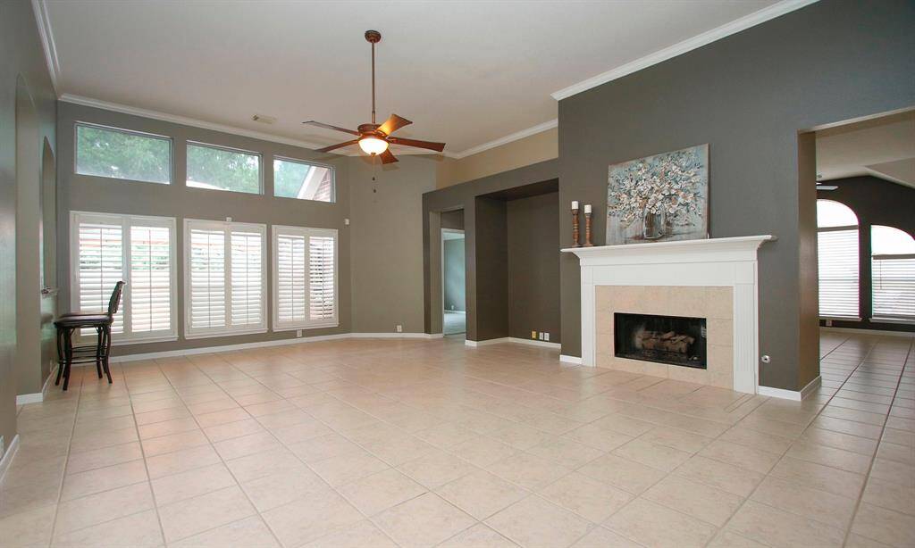 Spacious family room with tall ceiling, gas log fireplace, custom wall niche and wall-of-windows with plantation shutters.