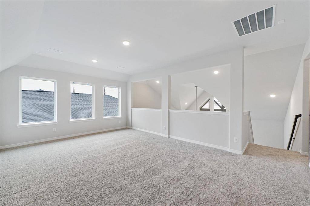 Bright and spacious game room area with soft carpeting, recessed lighting, and three large windows, offering a versatile space overlooking the main level below.