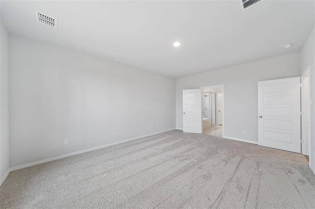 This spacious primary bedroom features neutral carpeting and a ceiling light. It connects to a bathroom through a double door, providing convenience and privacy.