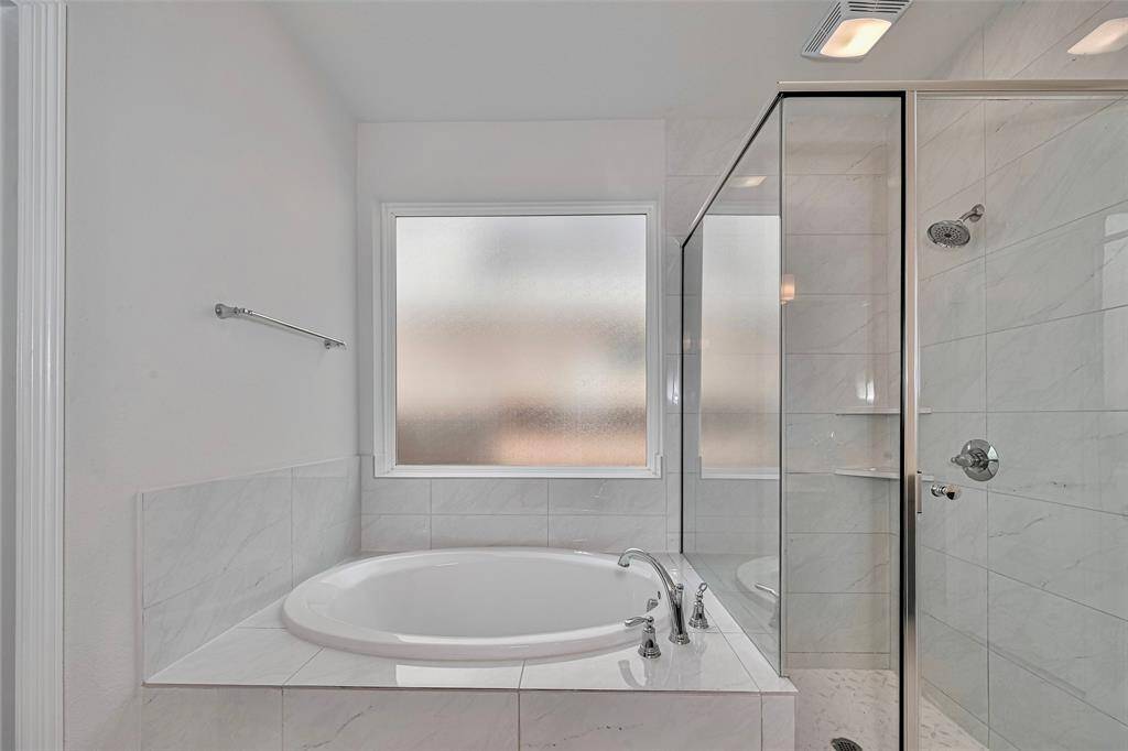 Soaking tub in primary bath features a glass-enclosed shower, and a large frosted window for natural light and privacy. The clean, white design and sleek fixtures create a bright and inviting space.