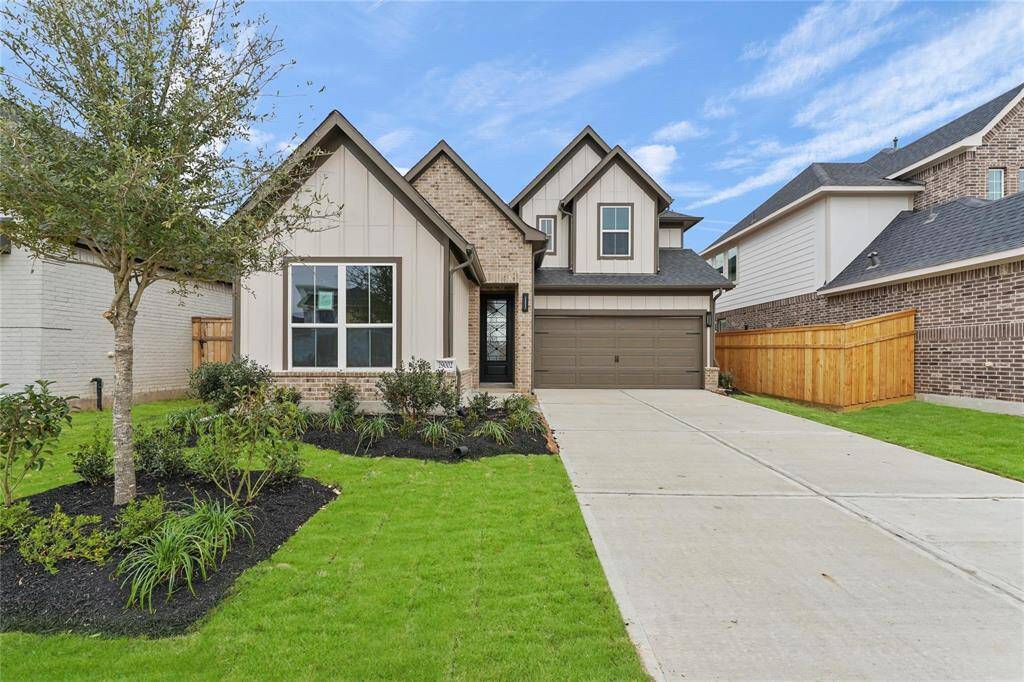 Welcome home! neatly landscaped front yard with a tree and shrubs, a spacious driveway leading to a two-car garage. The design is contemporary and inviting, perfect for family living.