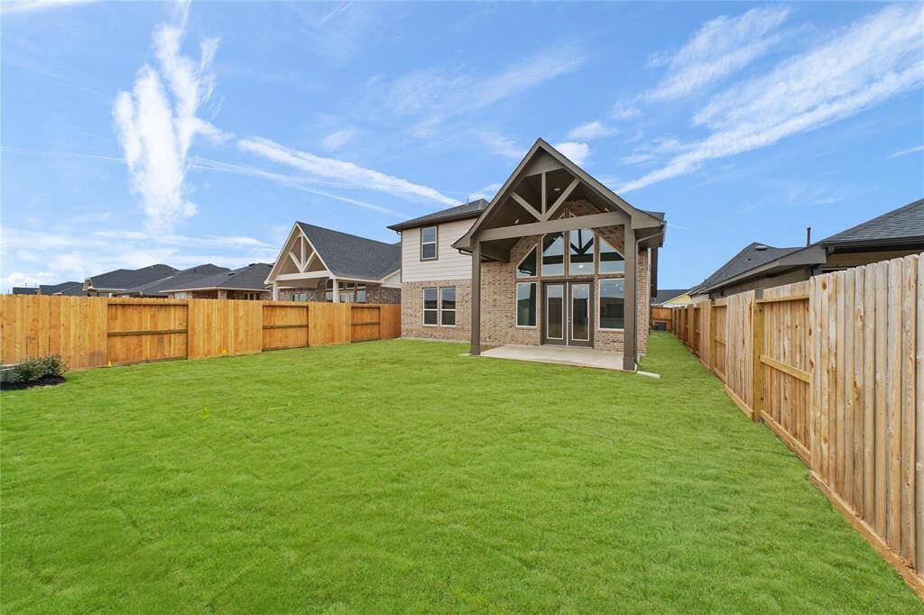 Spacious & well-maintained lawn enclosed by wooden fencing. The back of the house features a covered patio with large windows and a gabled roof, offering a modern, inviting outdoor space.