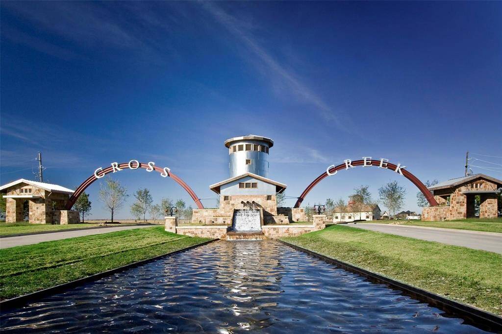 Cross Creek entrance featuring a striking water feature, stone structures, and an arched sign set against a clear blue sky. It's an inviting and picturesque community entrance.