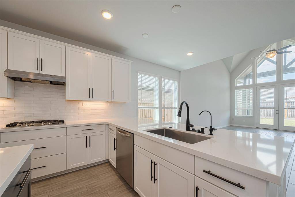 Modern open-concept kitchen and living area with high ceilings. Features include a central island, sleek cabinetry, stainless steel appliances, and large windows offering ample natural light.