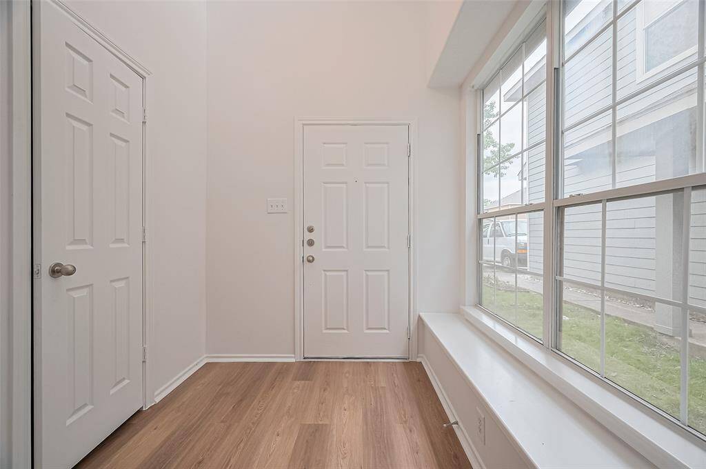 This entryway features a light, airy feel with large windows for natural light, wood flooring, and neutral walls. It includes a standard front door and a closet for storage.